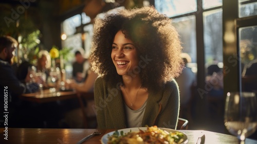 A young woman with curly hair is sitting in a restaurant  smiling.