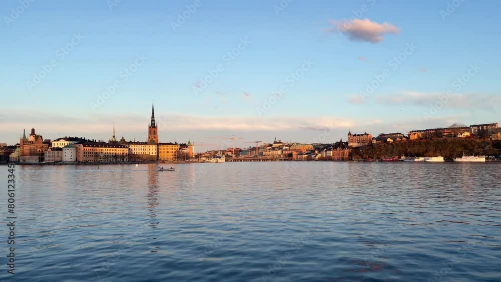 A small boat with the swedish flag passing infront of the island of Riddarholmen and the old town of Stockholm at sunset. The Slussen area and Södermalm district in the far distance. Clear sky. A small boat with the swedish flag passing infront of the island of Riddarholmen and the old town of Stockholm at sunset. The Slussen area and Södermalm district in the far distance. Clear sky.