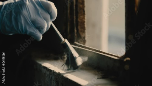 Person in blue gloves brushing black powder on windowsill