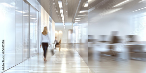 Blurred in motion office space office space with glass walls and workers passing by. A woman walks down a hallway with a briefcase in her hand.