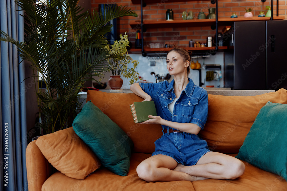 Obraz premium Young woman enjoying a peaceful moment on a cozy orange couch with a book and coffee cup