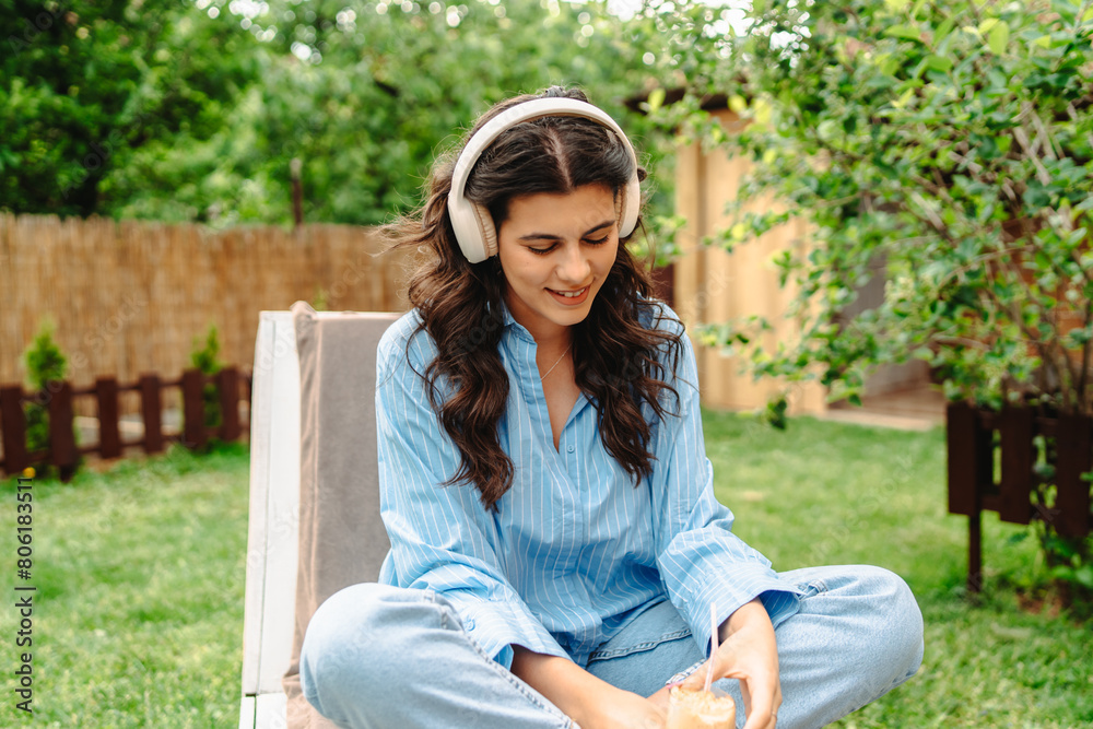 One young caucasian woman is enjoying music on her wireless headphones while laying on easy chair in her backyard One young caucasian woman is enjoying music on her wireless headphones while laying on easy chair in her backyard