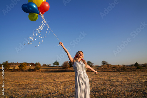 Young happy woman with balloons at sunset in summer. Happy woman running and having fun with balloons in nature at sunset