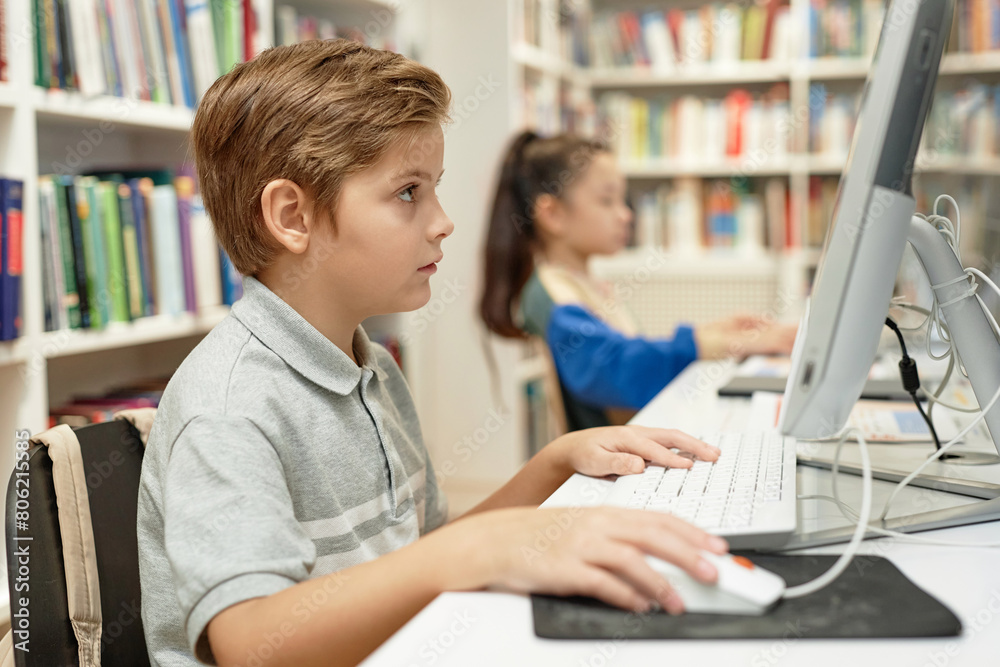 Side view portrait of serious young boy using PC computer in school library during programming class for kidswith copy space