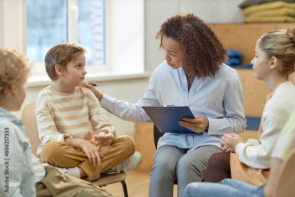 Fototapeta premium Side view portrait of young female psychologist comforting boy in support group for children and teenagers