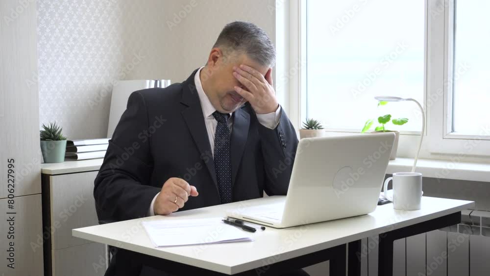 A tired man in an office setting yawns and rubs his eyes due to computer strain. Ideal for content for workplace health, preventing eye strain, and office wellness. A tired man in an office setting yawns and rubs his eyes due to computer strain. Ideal for content for workplace health, preventing eye strain, and office wellness.