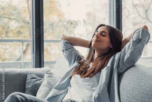 Relaxed serene pretty young woman feel fatigue lounge on comfortable sofa hands behind head rest at home, happy calm lady dream enjoy wellbeing breathing fresh air in cozy home modern living room.