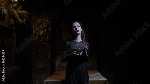 Portrait of mysterious fortuneteller shuffling Tarot cards standing in dark enigmatic room with flickering light and mystical atmosphere, looking at camera. Concept of esoteric, fortune telling.