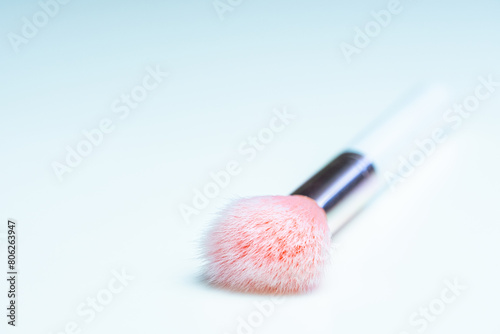 Close-up view of a makeup brush with pink bristles and a white handle on a clean white table