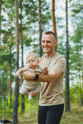 A young dad holds his little son in his arms while standing in the park. Dad is playing with his son