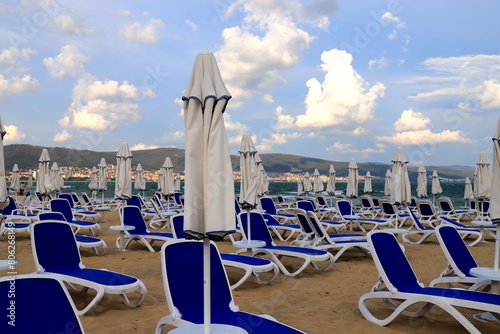 Beautiful beach on seashore, sun loungers stand on shore for sunbathing, people walk, play sports