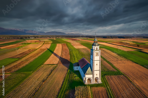 Aerial view of a colourful autumn sunset at the church of St. Ursula. St. Ursula's Church in the middle of the agricultural fields of Sorsko polje just before the autumn storm. Kranj, Slovenia photo