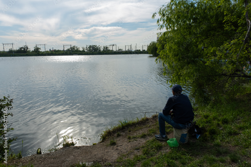 A man fishes in a lake in the city. Urban atmosphere on the shore of the lake