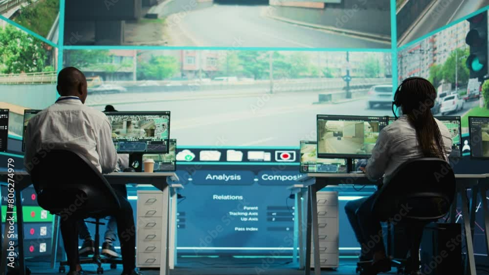 Diverse employees working on examining real time surveillance footage to find irregularities within urban traffic dynamics. Agency workers monitoring video on CCTV system for intelligence. Camera B. Diverse employees working on examining real time surveillance footage to find irregularities within urban traffic dynamics. Agency workers monitoring video on CCTV system for intelligence. Camera B.