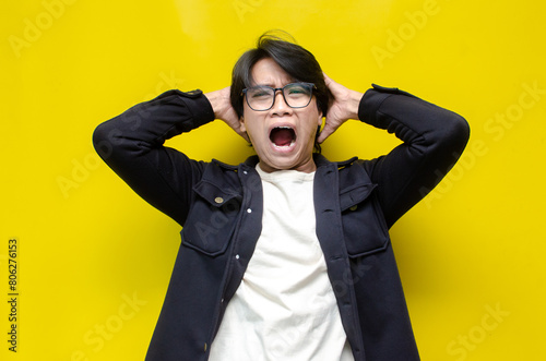 portrait of the anger expression of an Asian young man, threatening, accusing, and looking for fight. A hysterical, mad depressed indonesian young man hand, shouts and screams while grabbing hair
