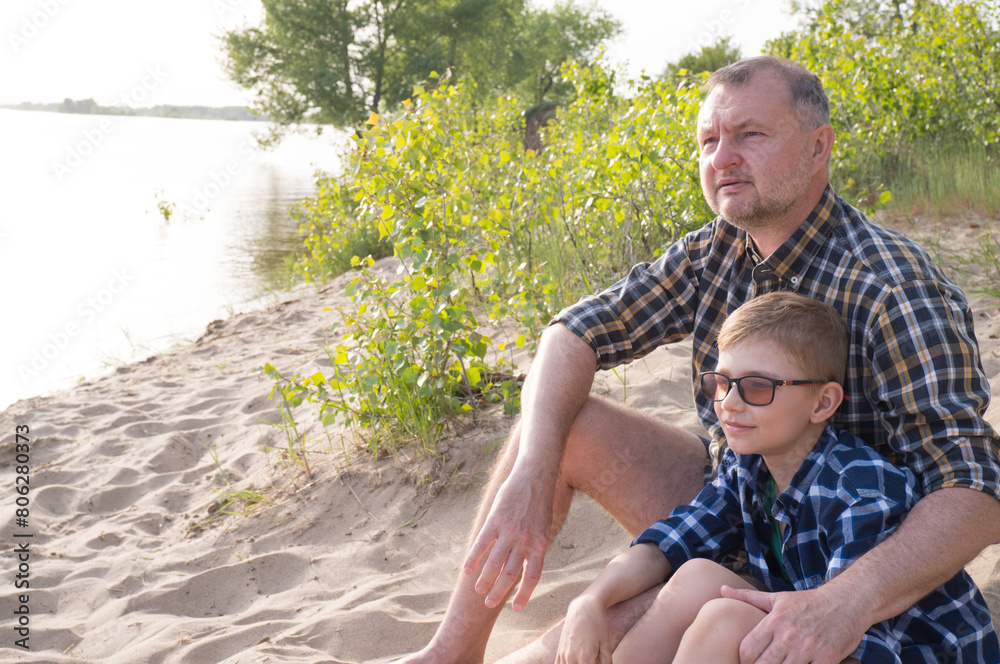 Father's day concept. Father and son sit together on the river bank and look into the distance.