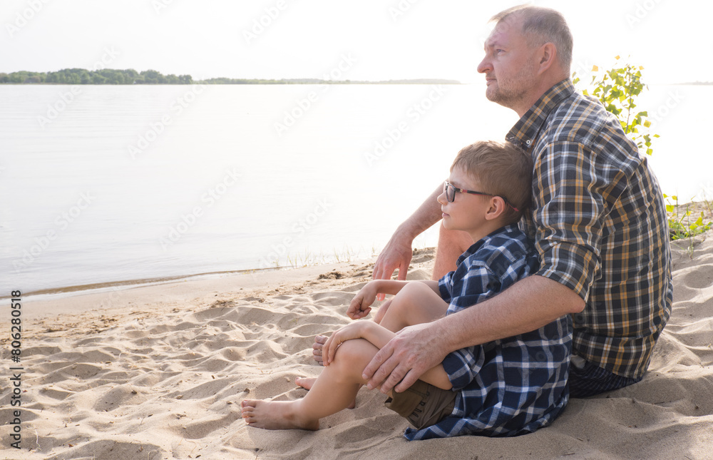 Father's day concept. Father and son sit together on the river bank and look into the distance.