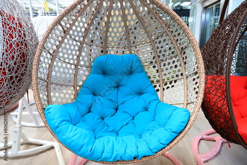 Rattan cocoon chair, garden furniture with blue cushion in store. Beautiful fashionable modern wicker furniture, sofa, rocking chair cocoon for interior
