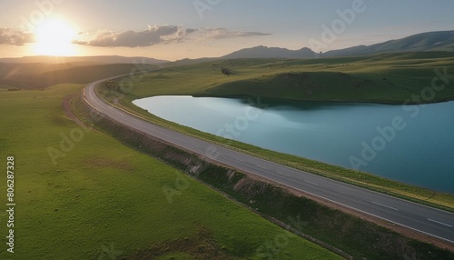 asphalt highway road and blue lake with green grass nature landscape at sunset