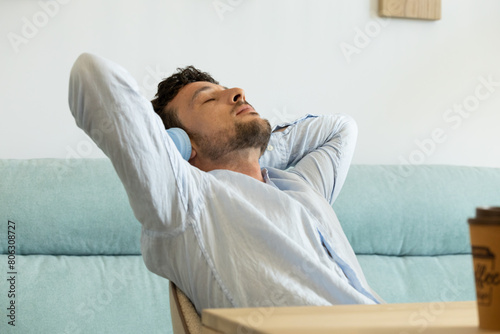 man relaxing after finishing work with his arms behind his head while listening to his favorite music on headphones