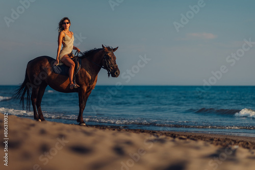 Beautiful young woman horseback riding on the beach during a summer sunset