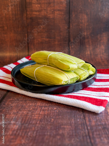 Peruvian sweet humitas, served in a black color plane on a wooden background. Wide angle shot. Green tamale. Vertical photo for social networks.