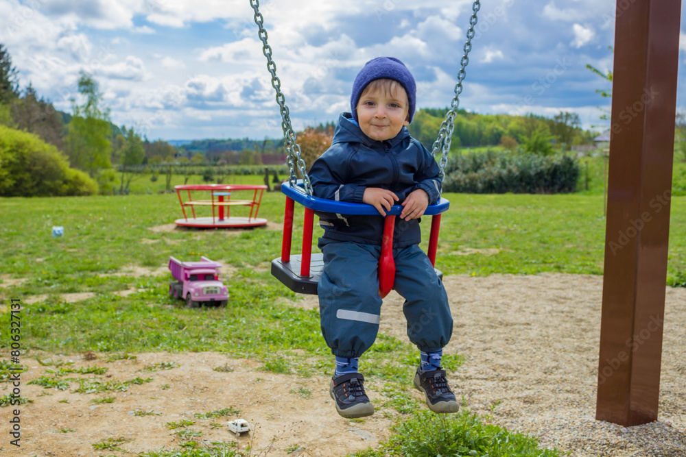 Little boy having fun on a red and blue swing on the playground on spring day. Little boy having fun on a red and blue swing on the playground on spring day.