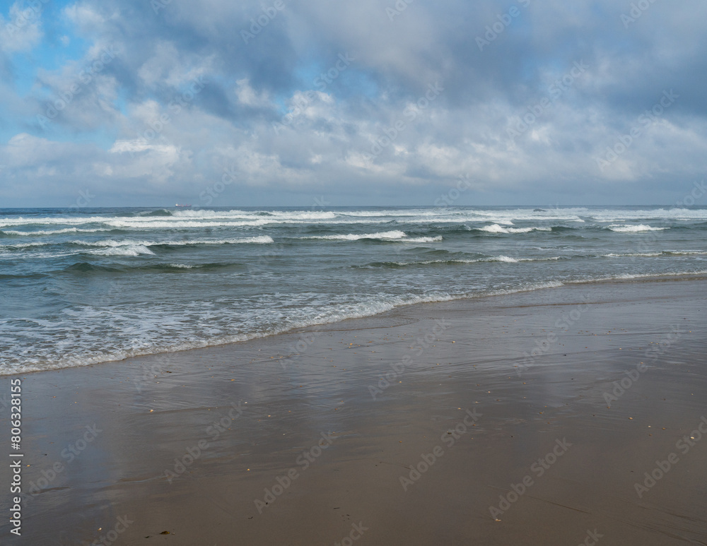The waves of the Atlantic Ocean wash the sandy beach, the horizon is visible, the day is overcast.	