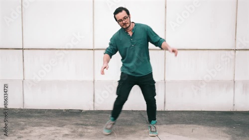 Stylish young man in teal shirt performing street dance with expressive hand movements against a white tile background.