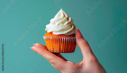 Trendy minimalist photo of a hand holding a cupcake against a muted mint background