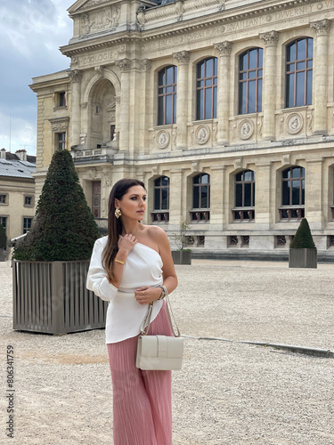 beautiful woman with dark hair in elegant clothes with accessories posing in beautiful Paris garden with beautiful monument