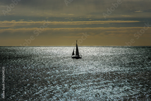 Backlit image of a sailboat sailing in the Atlantic Ocean, with a beautiful sky as a background and the sea with its shiny surface. © phjacky65