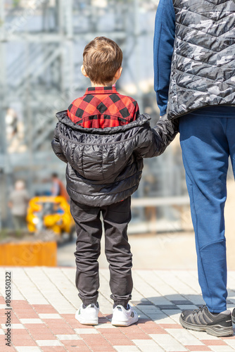 A boy holds his father's hand. Back view of a small child. Unknown future. Parental support. A single father. An orphan child. An adult and a child. Childhood in Ukraine. Protection of children.