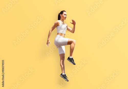 Athletic woman jumps energetically in sportswear against yellow backdrop