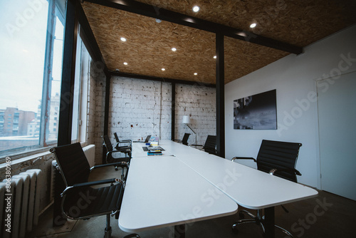 Modern spacious stylish office in loft style. Meeting room with a large wooden table near a large window. Workspace without people.