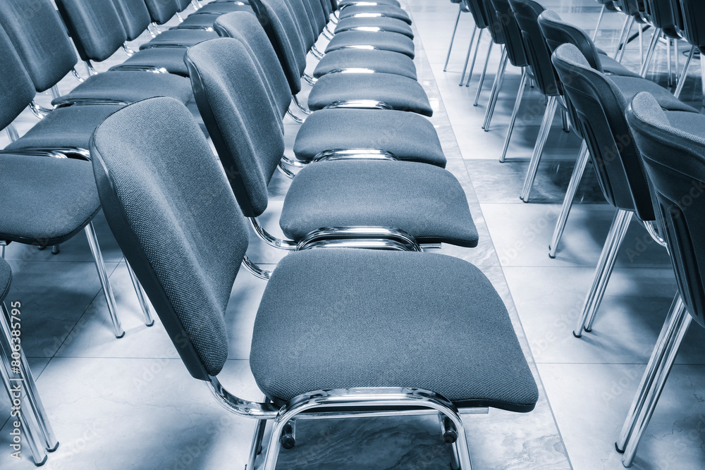 Fototapeta premium A row of chairs are empty in a room. The chairs are all the same color and are arranged in a line. The chairs are all facing the same direction, which gives the room a sense of order and organization