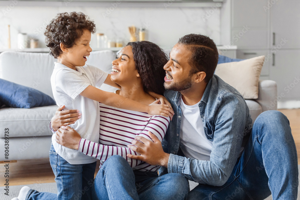Fototapeta premium African American man, woman, and child are seated on the floor in front of a couch. They appear to be engaged in conversation or possibly watching something together.