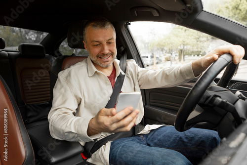 Cheerful middle aged driver man texting on smartphone while driving, sitting in car inside, male with gps navigator application navigating automobile © Home-stock