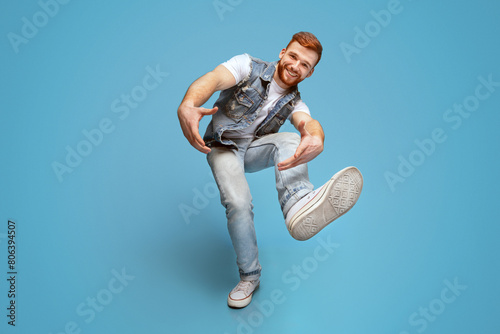 Come on! Smiling millennial caucasian guy fool around and marked out with hands at camera, full length, blue studio background