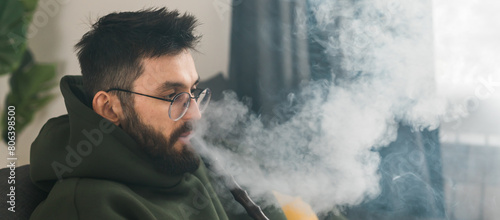 Banner bearded millennial or gen z man smoking hookah while relaxing on sofa at home copy space - chill time and resting concept photo