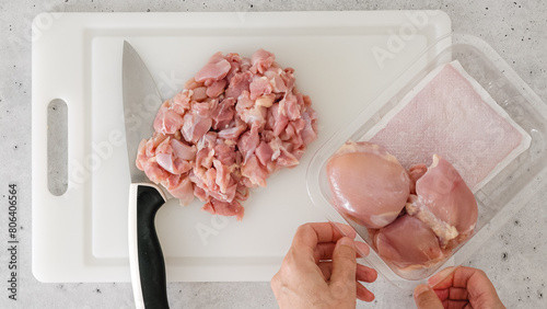 Chopped raw chicken fillet close-up on a white plastic cutting board. The chef cuts meat, close-up preparation process, recipe photo