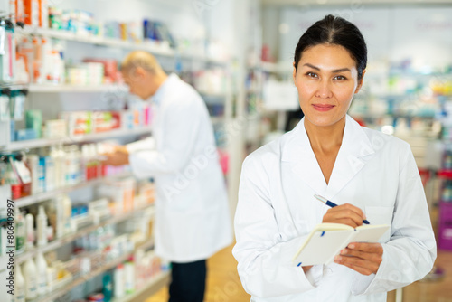 Positive female pharmacist makes notes on a notebook in the sales area of a pharmacy