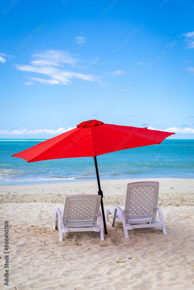 Two empty beach chairs and an umbrella on a beautiful day in the Caribbean