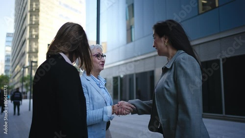 Group of mature business women close a deal by shaking hands outside corporate office. Three professional formal female talking confidently outdoors. Feminine empowered meeting lawyers  photo