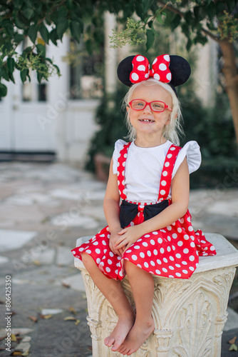 Fotografía little blond girl in red polka dot dress and Minnie Mouse ears with red glasses
