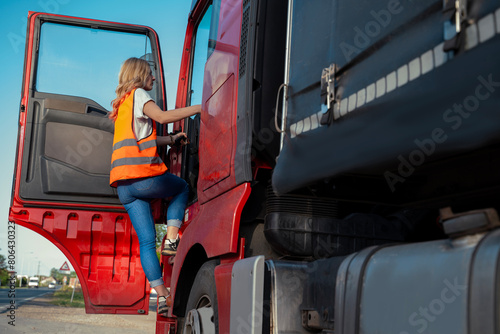 Woman truck driver with safety vest entering a cabin, shot from outside the truck 