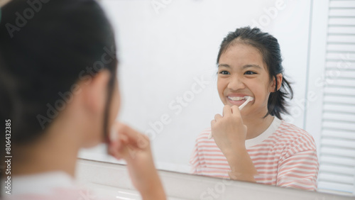 A young girl is brushing her teeth in front of a mirror