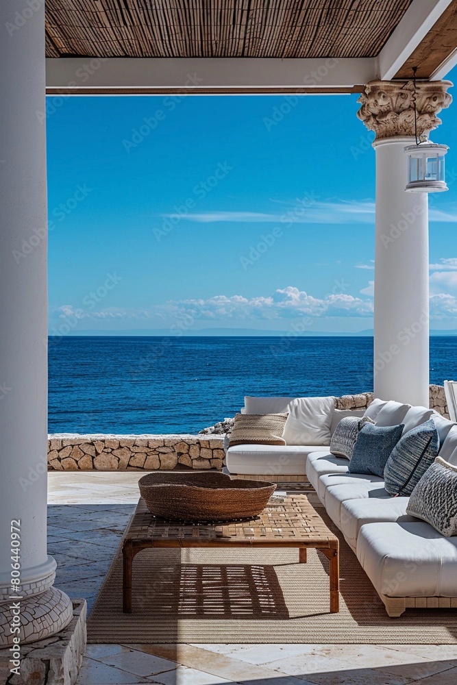 Fototapeta premium vila, a covered outdoor lounge area with a plush sofa, woven accents, and a stunning view of the turquoise sea framed by a classical column