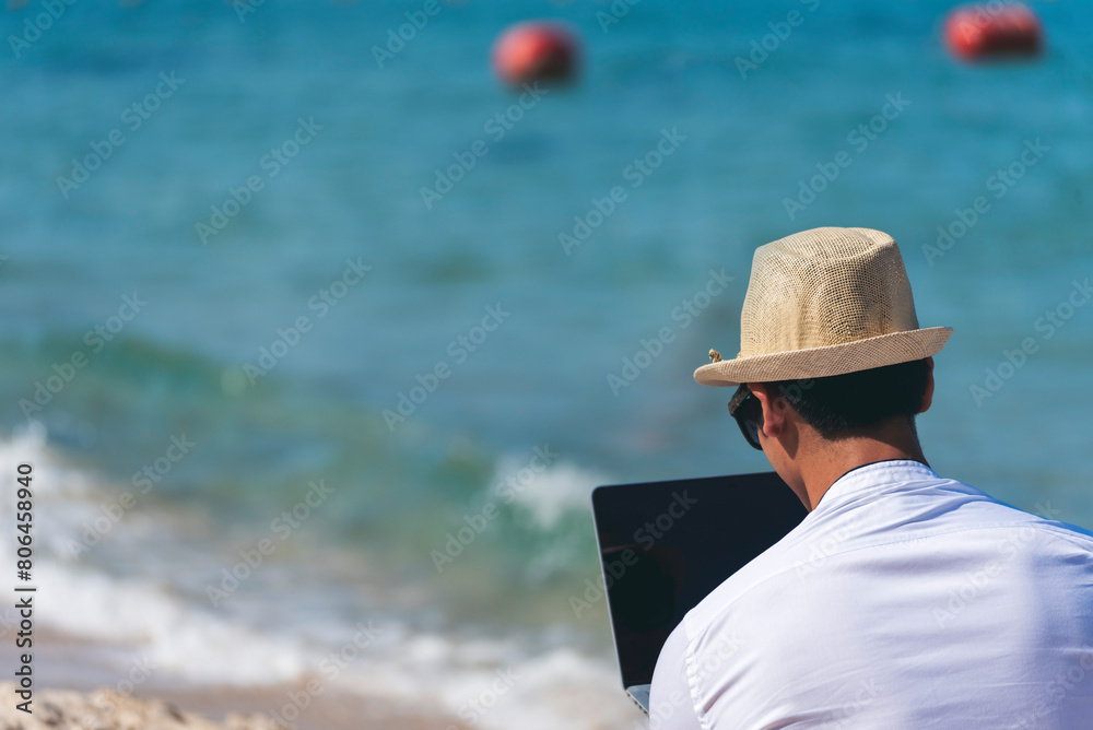 Man traveler use laptop on summer beach blue sky. Asian man wear casual short pants tropical shirt style relax on the beach in summertime. Man typing laptop computer  holiday business trip