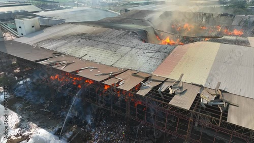 From above, witness a fierce conflagration ravaging an industrial structure. Flames dance amidst ruins, devouring all in their path. Smoke billows, obscuring the horizon in a haze of devastation.
